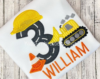 May include: A white t-shirt with a yellow construction hat, a black number 3 with a gray road design, a yellow construction vehicle, an orange traffic cone, and the name "WILLIAM" in orange letters.