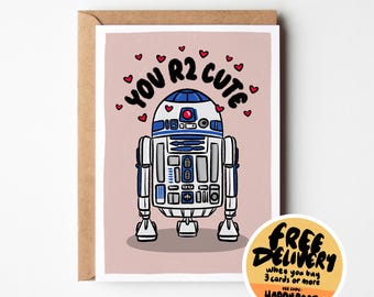 Puede incluir: Una tarjeta de felicitación con una ilustración de dibujos animados de R2-D2 y el texto "YOU R2 CUTE" con forma de corazón. La tarjeta está sobre un fondo rosa, con un sobre marrón. Una pegatina redonda dice "ENTREGA GRATUITA".