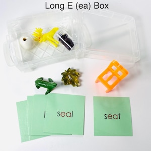 May include: A clear plastic box labeled "Long E (ea) Box" containing small toys and flashcards. The box holds a yellow moose, a white bead, a green frog, and other items. Flashcards display the words "seal" and "seat".