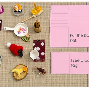 Peut inclure: Une collection d'objets miniatures comprenant un sac à main rose, une souris blanche, une tasse jaune, une casquette bleue, une figurine de renard, une toupie, une poêle blanche, un chapeau rouge, une figurine de chien, un insecte et des cartes roses avec le texte Put the bat in the hat et I see a bag on a tag.