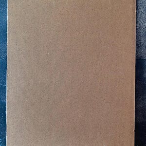 May include: A rectangular, brown, textured board with a woven pattern. The board is set against a dark blue background. The board's surface has a consistent, fine texture.