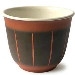 Puede incluir: Una maceta de cerámica de color terracota con una banda marrón oscura y líneas verticales. La maceta tiene una forma redonda y lisa y un interior blanco.