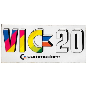 Op de afbeelding: Een vintage sticker voor de Commodore VIC-20 computer met een kleurrijk logo en de tekst "VIC-20" en "Commodore".