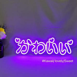 May include: Purple neon sign with the Japanese word "kawaii" written in white, with hearts on either side of the word. The sign is on a purple background with the text "#Kawaii/lovely/Sweet" below it.