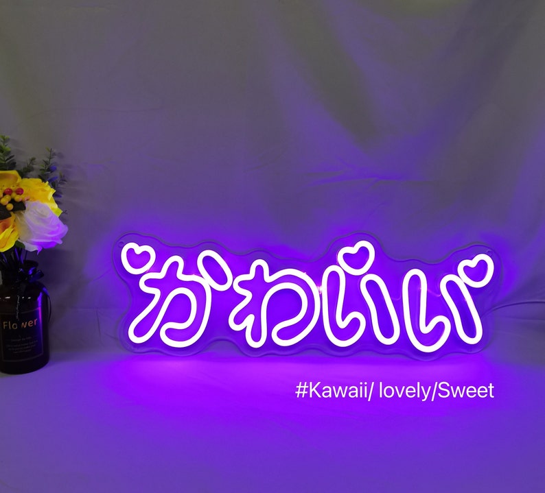 May include: Purple neon sign with the Japanese word "kawaii" written in white, with hearts on either side of the word. The sign is on a purple background with the text "#Kawaii/lovely/Sweet" below it.