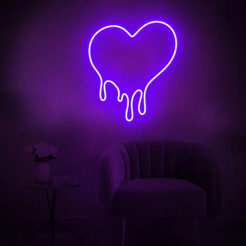 May include: Purple neon sign shaped like a dripping heart. The sign is mounted on a wall behind a purple velvet armchair.