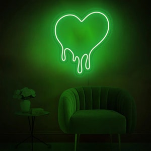 May include: A green neon sign shaped like a dripping heart. The sign is mounted on a wall behind a green velvet armchair.