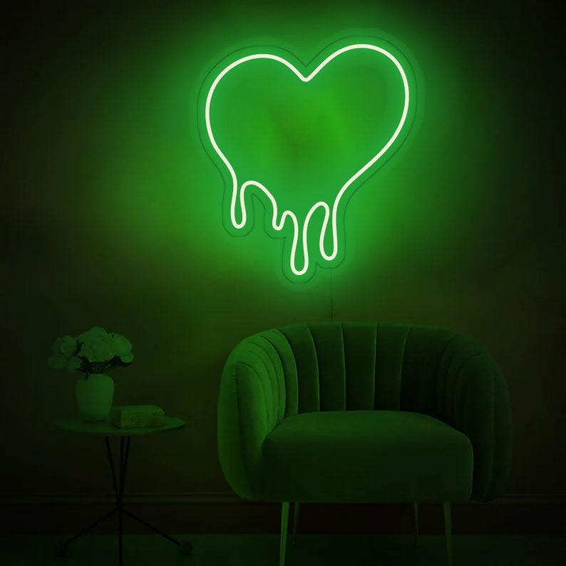 May include: A green neon sign shaped like a dripping heart. The sign is mounted on a wall behind a green velvet armchair.