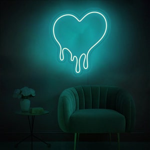 May include: A teal blue neon sign shaped like a dripping heart. The sign is mounted on a wall behind a teal blue velvet armchair.