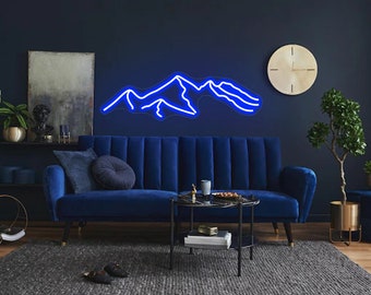 May include: A blue neon sign depicting a mountain range, hanging on a dark blue wall above a blue velvet sofa. The sofa is in a living room setting with a coffee table and a potted plant.