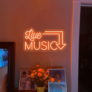 Op de afbeelding: Een oranje neonbord met de woorden "Live Music" in een witte omtrek. Het bord is gemonteerd aan een muur met een wit snoer.