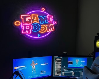 Puede incluir: Un letrero de neón con las palabras "GAME ROOM" en un esquema de colores rosa, azul y naranja. El letrero está montado en una pared oscura.