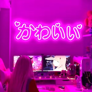 May include: Pink neon sign featuring the Japanese text "kawaii" in a playful, rounded font. The sign is lit up and has small heart shapes around the text.