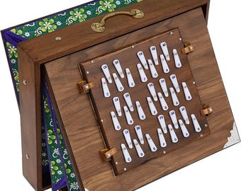 May include: A portable wooden harmonium instrument featuring a dark brown finish, a brass handle, and a bellows section lined with green and purple floral fabric. The front panel displays white keys labeled with musical notes including C, D, E, F, G, A, B.