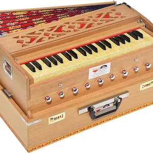 May include: A wooden harmonium with a keyboard of black and white keys, red accents, and silver knobs. The instrument has a decorative patterned top and a handle for carrying. The brand name "Kanya Musicals" is visible.