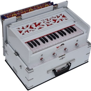 May include: A white harmonium with a floral design on the top and a black keyboard. The harmonium has a built-in carrying handle and is closed. The brand name "Kadyana Music" is visible on the side.