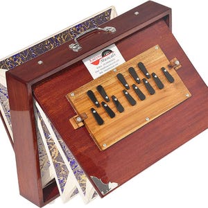 May include: A red wooden harmonium with a decorative inlay of blue and gold. The harmonium has a row of black keys and a label that reads "Kaavya Musicals".