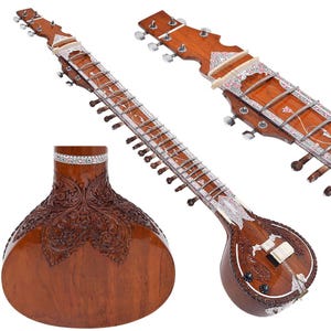 May include: A brown sitar with intricate carvings and silver accents. The instrument features a long neck with frets, multiple strings, and a rounded body. The headstock has tuning pegs. The sitar is a traditional Indian stringed instrument.