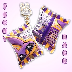 Puede incluir: Un llavero morado y amarillo con forma de caramelo con un cierre en forma de conejito. La parte delantera del envoltorio del caramelo presenta una cara de dibujos animados con estrellas, mientras que la parte trasera muestra información nutricional y un código de barras.