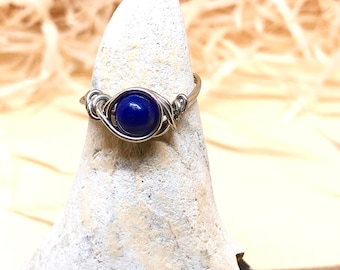 May include: A silver wire wrapped ring with a dark blue gemstone.