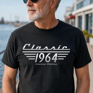 Peut inclure: Un t-shirt noir à manches courtes avec une impression graphique argentée sur la poitrine. Le motif affiche le mot Classic au-dessus du nombre 1964, encadré par des lignes horizontales, avec le texte Limited Edition en plus petite police.