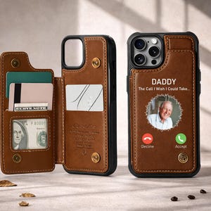 May include: A brown leather phone case with a wallet. The case has a black frame and a snap closure. The wallet section holds cards and cash. The phone screen displays a photo and the words "DADDY" and "The Call I Wish I Could Take..."