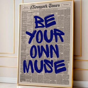 以下が含まれることがあります： ヴィンテージ新聞を背景に、「BE YOUR OWN MUSE」という言葉が太字の青い文字で書かれた額入りのプリント。プリントは金色のフレームで額装されています。新聞の見出しには「The Newyork Times」と書かれています。壁の装飾に最適です。