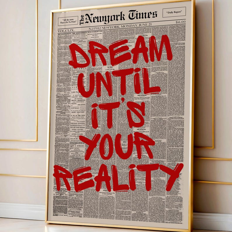 以下が含まれることがあります： ヴィンテージ新聞を背景に、「DREAM UNTIL IT'S YOUR REALITY」という赤い文字が書かれた額入りのプリント。プリントは金のフレームに入っています。モチベーションを高めるアート作品。