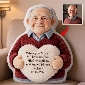 May include: A custom-shaped pillow resembling an elderly man, wearing a burgundy sweater and a light blue collared shirt. The pillow holds a heart-shaped cushion with the text "When you MISS ME have no fear HUG this pillow and know I'M here Robert 1960-2025."
