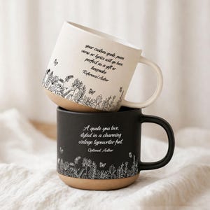 May include: Two ceramic mugs, one white and one black, stacked together. The white mug has a floral design and text that reads "your custom quote, poem verse or lyrics will go here." The black mug has a similar floral design and text that reads "A quote you love."