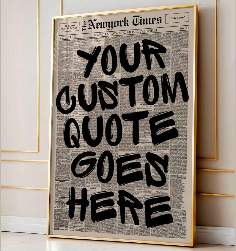 以下が含まれることがあります： 新聞の背景に「YOUR CUSTOM QUOTE GOES HERE」というテキストが黒い太字で書かれた額入りのプリント。フレームは金色で、プリントはニュートラルな壁に飾られています。