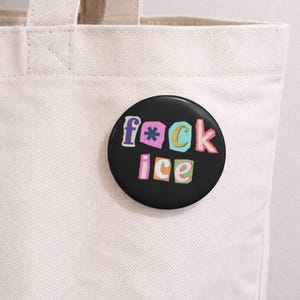 Könnte beinhalten: Ein schwarzer Button mit den Worten "f*ck ice" in bunten, ausgeschnittenen Buchstaben. Der Button befindet sich vor einer weißen Tragetasche.