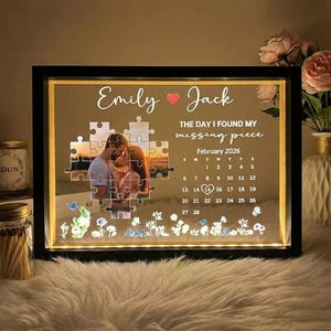 May include: A black framed illuminated photo display with the names "Emily" and "Jack" and the text "THE DAY I FOUND MY missing piece". The photo features a couple in a puzzle piece design, with a calendar for February 2026.