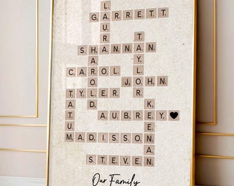 May include: Framed family name art featuring names spelled out in a crossword puzzle style. The names are on individual letter tiles, with a black heart tile. The words "Our Family" are written in cursive at the bottom. The frame is gold.