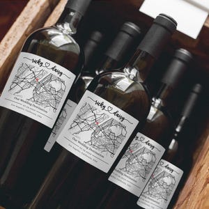May include: Several wine bottles in a wooden crate. Each bottle has a label with a map design, the names "ricky ♡ daisy", and the text "Our Wedding Destination 07.18.2019 Los Angeles, California, USA". The bottles are dark with black caps.