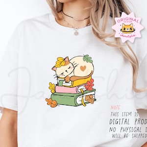 Op de afbeelding: Wit T-shirt met een cartoonkat die op boeken slaapt, versierd met herfstbladeren. De kat is cr&egrave;mekleurig met een geel blad op zijn hoofd en een hart op zijn zij. De tekst op het shirt luidt: "NOTE THIS ITEM IS DIGITAL PRODUCT. NO PHYSICAL ITEM WILL BE SHIPPED."
