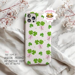 May include: A white phone case with a pattern of green four-leaf clovers with pink bows. The case has a camera lens cutout and a white background. The text "ORIGINAL DESIGN Zanatshie" is on the case.