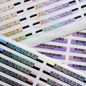 Peut inclure: Gros plan sur des feuilles d'autocollants holographiques avec des codes-barres, des numéros de série et du texte. Les autocollants ont un aspect métallique irisé, reflétant des couleurs comme le violet et le vert. Les codes-barres sont noirs.