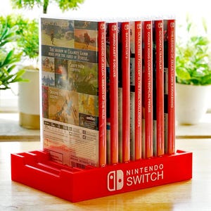 Può includere: Un porta-custodie per giochi Nintendo Switch rosso con un logo Nintendo Switch bianco. Il porta-custodie è pieno di varie custodie per giochi Nintendo Switch, tra cui The Legend of Zelda: Breath of the Wild, Mario Kart 8 Deluxe e Octopath Traveler.