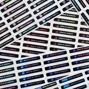 Może przedstawiać: Arkusz czarnych i holograficznych naklejek z tekstem i logo. Naklejki wyświetlają tekst "SERIAL No. HU0221013" oraz logo PlayStation, Sega i PSP.