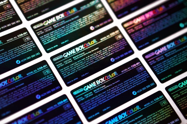 May include: Close-up of multiple black and iridescent holographic stickers with the text "GAME BOY.COLOR" and model number "CGB-001". The stickers also include the text "Nintendo" and "Made in Japan".