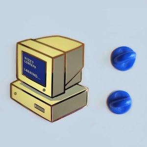 May include: A pin featuring a retro computer design with the text "Dizzy Leopard Loading..." on the screen. The pin has a yellow and gray color scheme with a blue screen. Two blue pin backs are also visible.