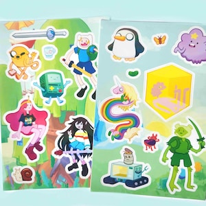以下が含まれることがあります： フィン、ジェイク、BMO、プリンセス・バブルガムなどの様々なキャラクターが描かれた、アドベンチャー・タイムのステッカー2枚。ステッカーはカラフルで、剣、虹色のユニコーン、ペンギンの画像が含まれています。