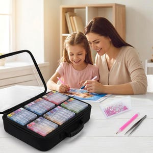 May include: A black storage case with a clear lid containing multiple small rectangular containers filled with colorful beads, alongside a pink applicator pen, a pair of metal tweezers, and a small tray of pink beads for diamond painting.