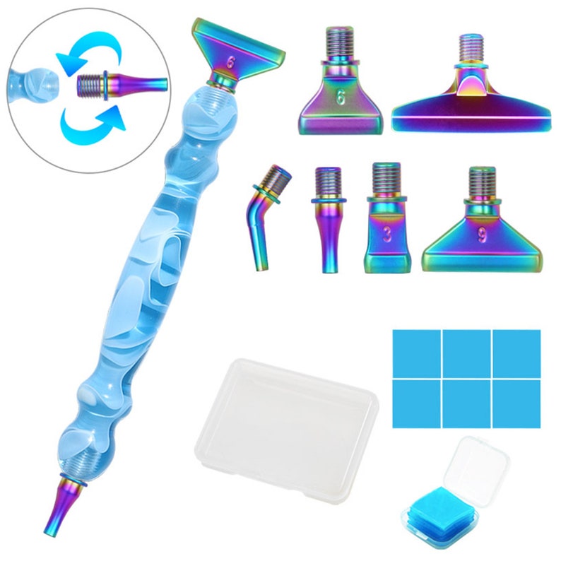 May include: A diamond painting pen set with a clear blue handle and iridescent tips. The set includes multiple interchangeable tips, a small clear container, and blue adhesive squares. The pen handle has a swirling white design.