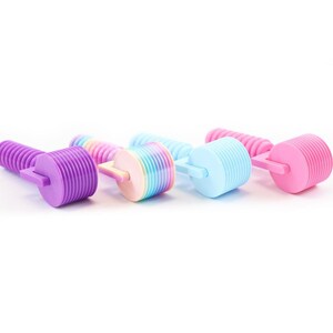 Puede incluir: Un conjunto de cuatro herramientas de rodillo de pl&aacute;stico para arcilla o masa, cada una con un cabezal cil&iacute;ndrico con crestas horizontales y un mango. Los rodillos son de color morado, un degradado arco&iacute;ris pastel, azul claro y rosa s&oacute;lido.
