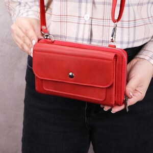 May include: A vibrant red rectangular crossbody wallet featuring a front flap with a single silver-tone snap button closure, a top zipper, and a matching red adjustable shoulder strap attached with silver-tone metal hardware clips.