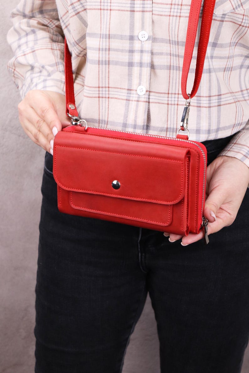 May include: A vibrant red rectangular crossbody wallet featuring a front flap with a single silver-tone snap button closure, a top zipper, and a matching red adjustable shoulder strap attached with silver-tone metal hardware clips.