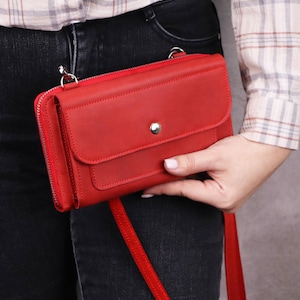 May include: A rectangular red leather crossbody bag featuring a front flap with a silver-toned snap button closure, a top zipper, and a matching red shoulder strap. The bag has a smooth matte finish and silver metal hardware attachments.