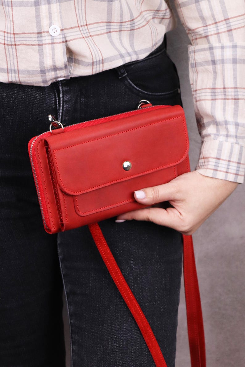 May include: A rectangular red leather crossbody bag featuring a front flap with a silver-toned snap button closure, a top zipper, and a matching red shoulder strap. The bag has a smooth matte finish and silver metal hardware attachments.